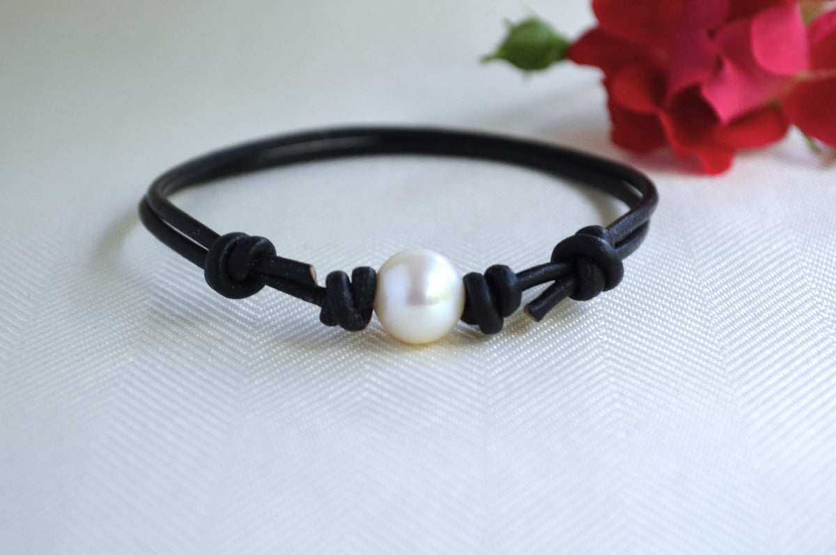 Black cord bracelet with a white pearl on a white background with red flowers.