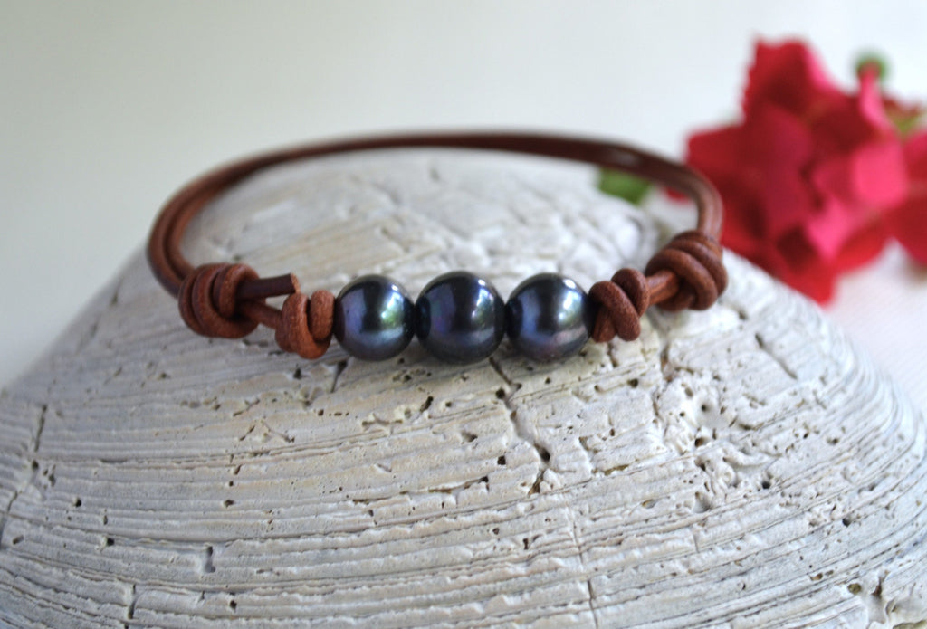 Bracelet with black pearls and brown leather strap on a textured surface with red flowers in the background
