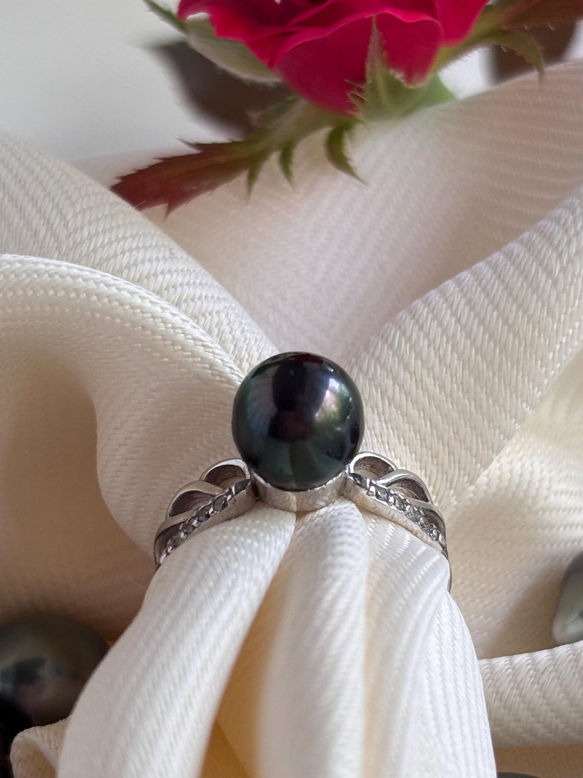 Pearl ring on a white fabric with a red flower in the background