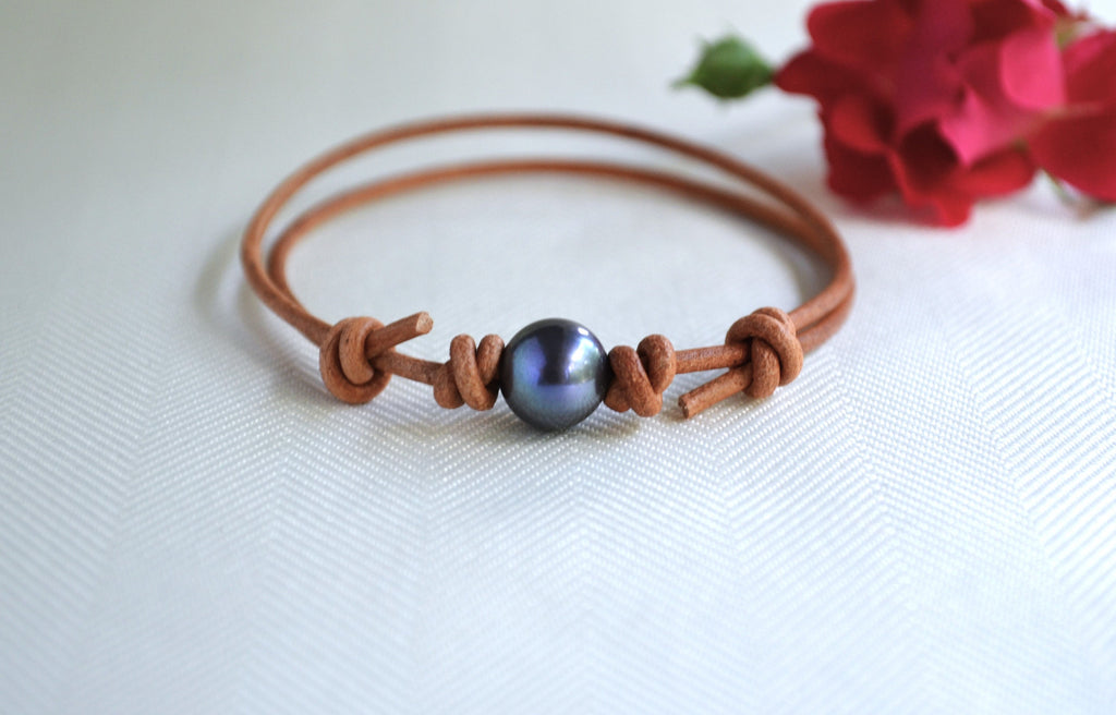 Brown leather bracelet with a blue pearl bead on a white background with red flowers.