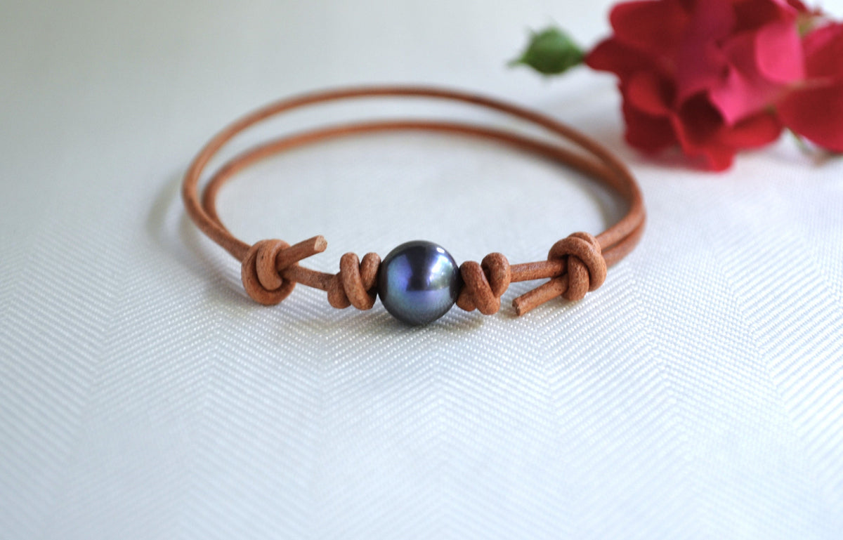 Brown leather bracelet with a blue pearl bead on a white background with red flowers.