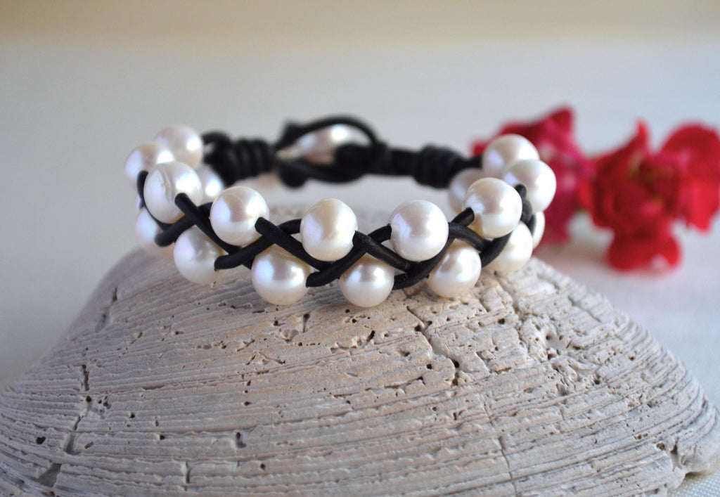 Pearl bracelet with black cord on a textured surface with red flowers in the background