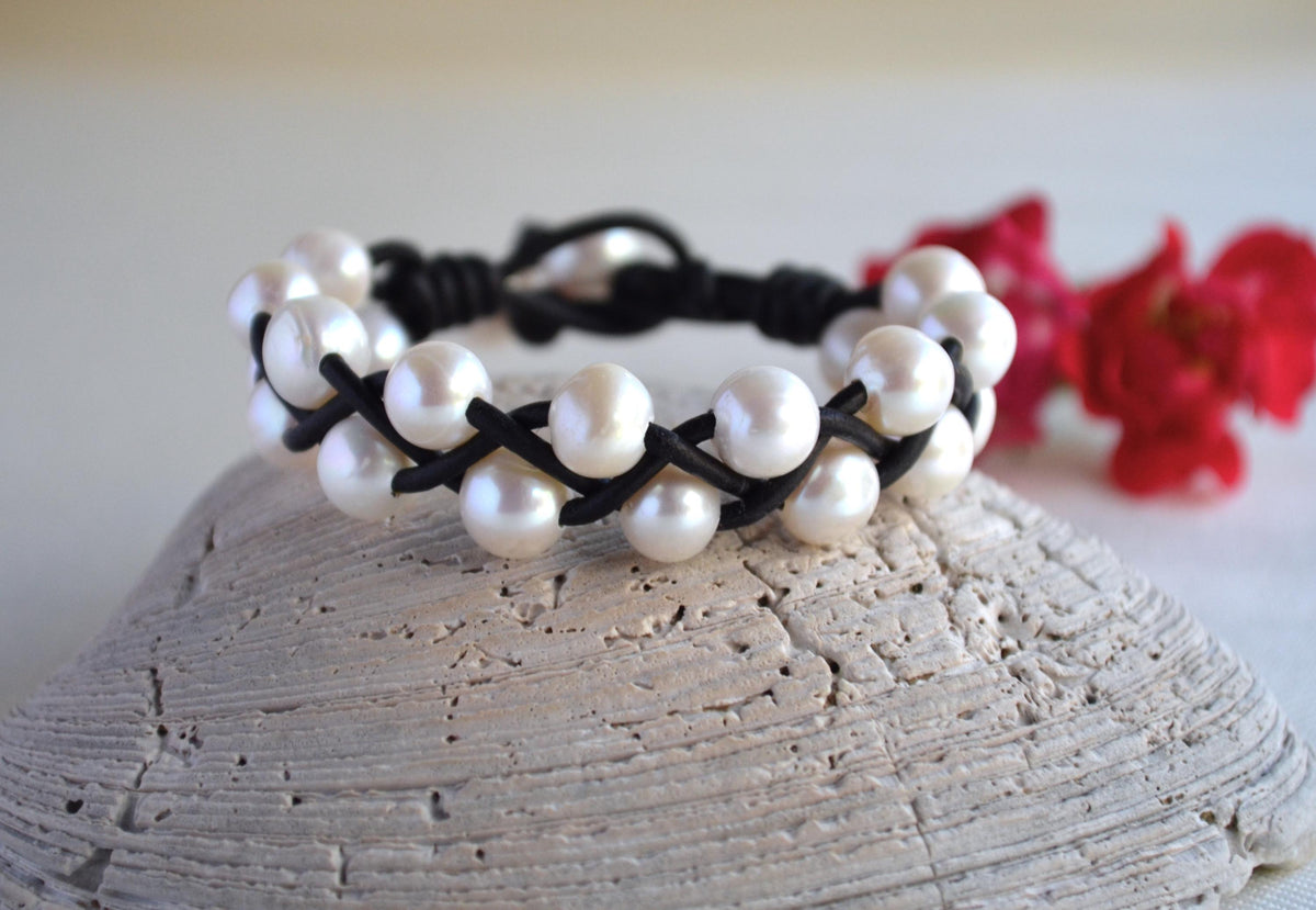 Pearl bracelet with black cord on a textured surface with red flowers in the background