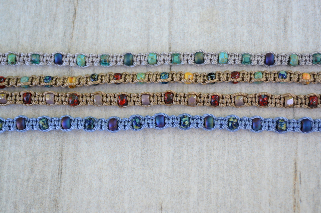 Four colorful beaded bracelets on a textured white background