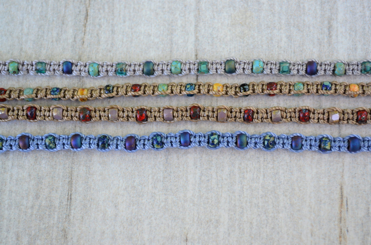 Four colorful beaded bracelets on a textured white background