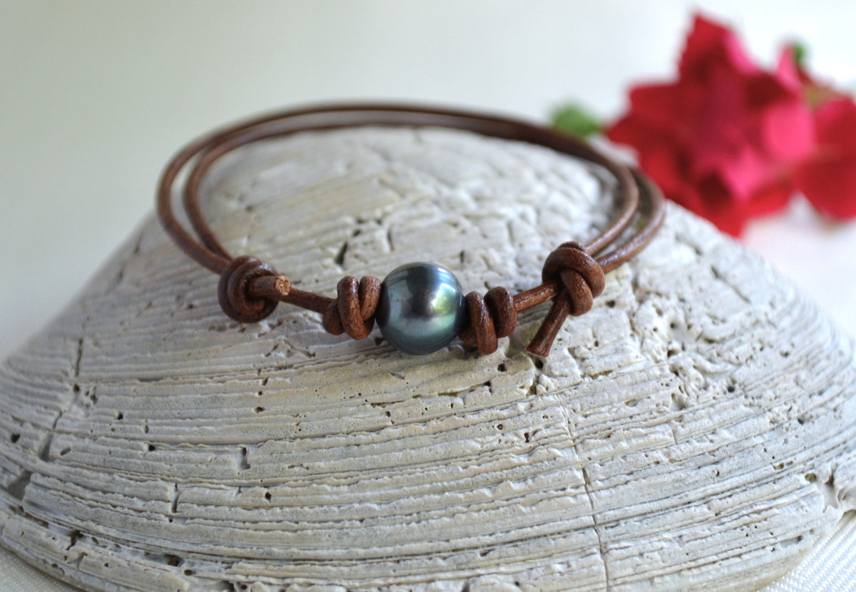 Bracelet with a blue pearl on a textured surface with red flowers in the background