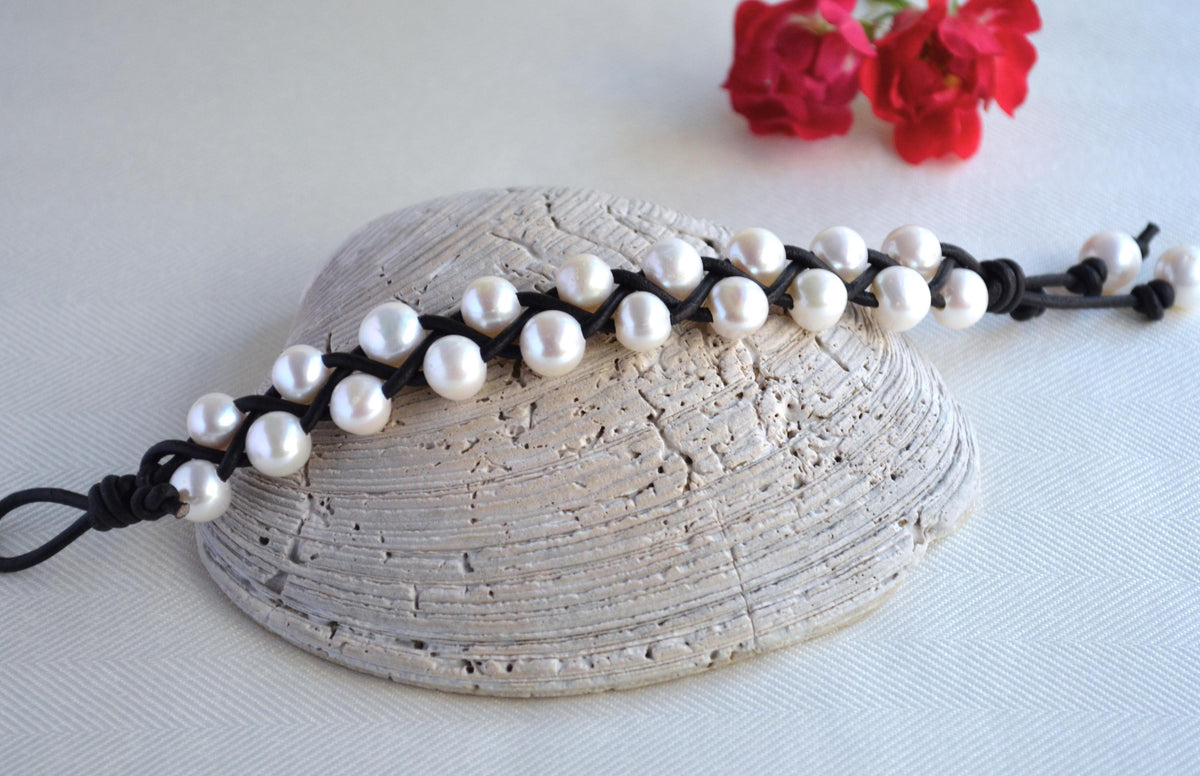 Pearl bracelet on a shell with red flowers in the background