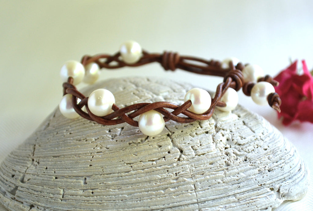 Pearl bracelet on a shell with a blurred pink flower in the background