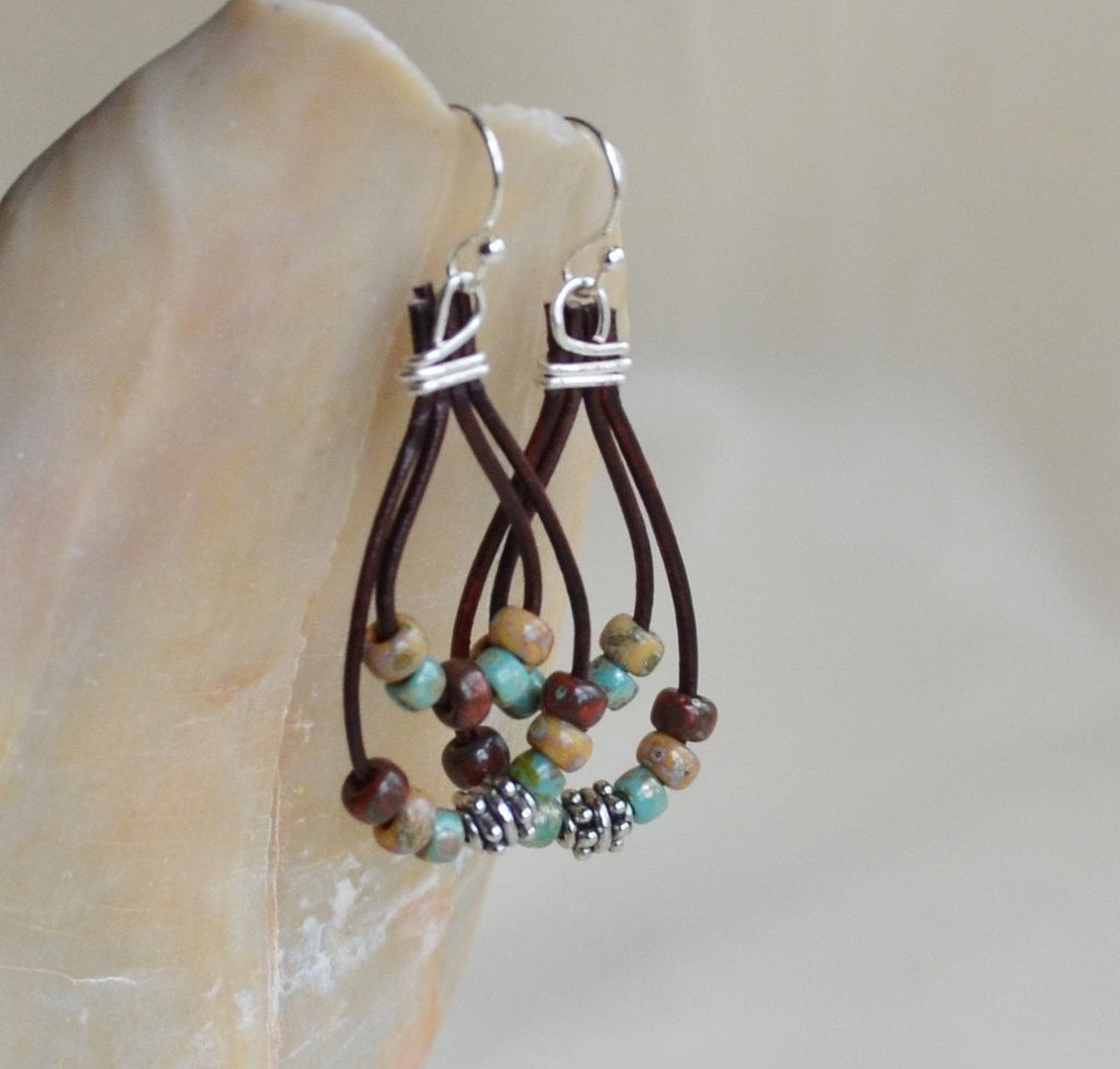 Beaded earrings with brown leather straps on a stone surface