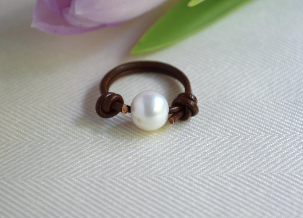 Pearl leather ring on a textured white surface with a blurred pink flower in the background