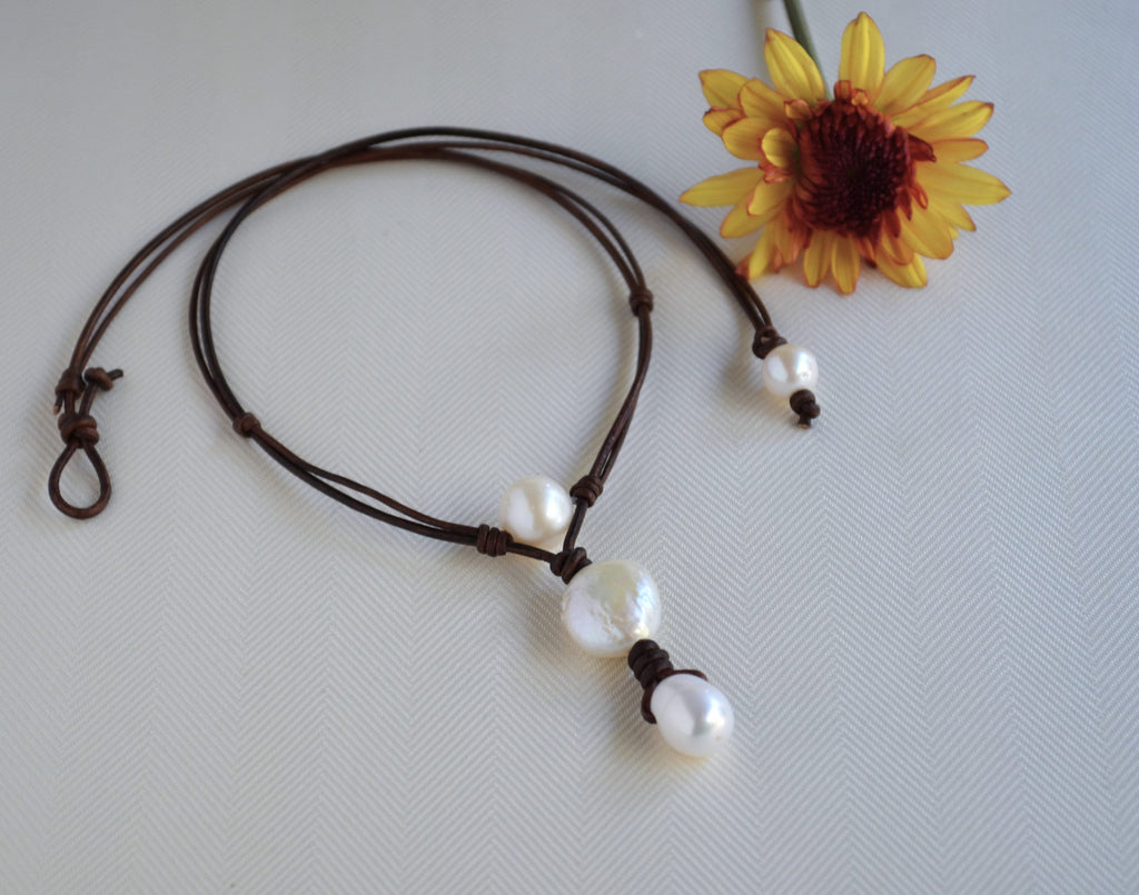 Necklace with white beads on a brown cord next to a yellow flower on a light gray background