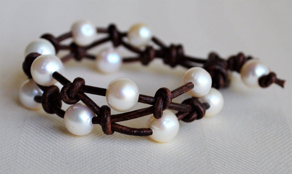 Two pearl bracelets with brown leather straps on a light background