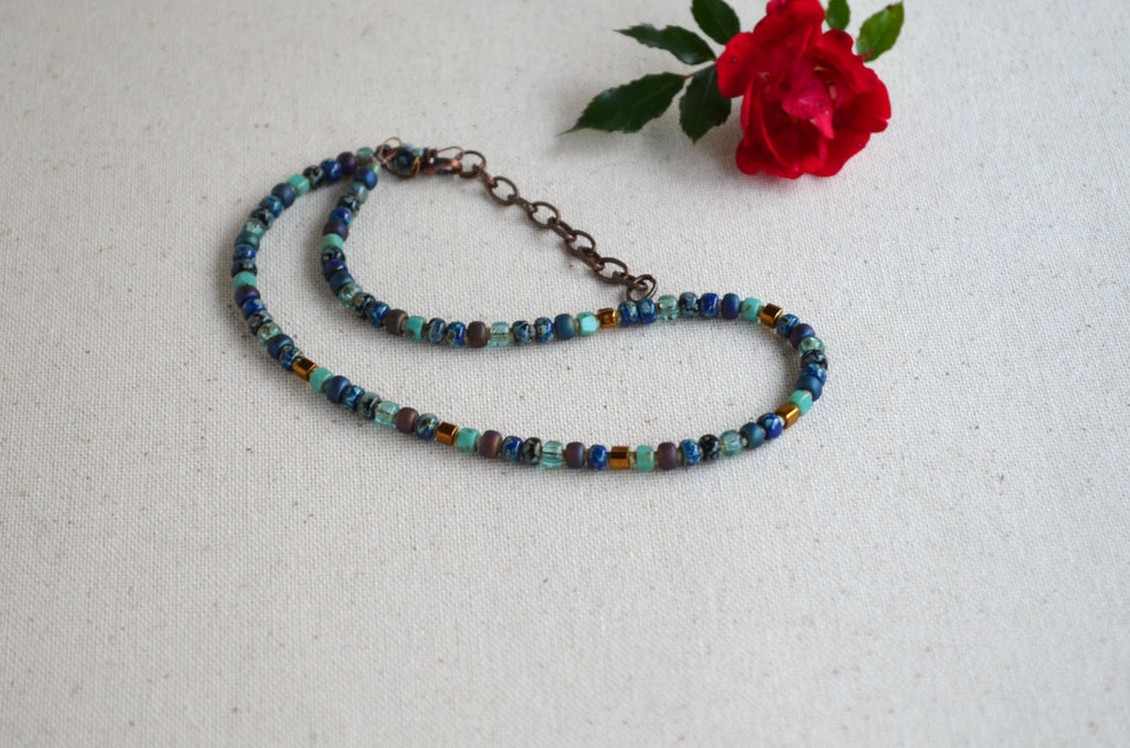 Beaded necklace on a textured surface with a red rose.