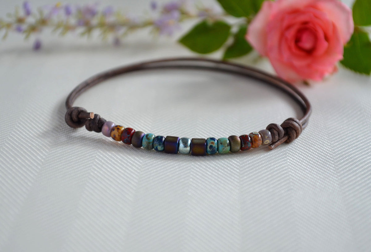 Multicolored beaded ankle bracelet on a white surface with flowers in the background