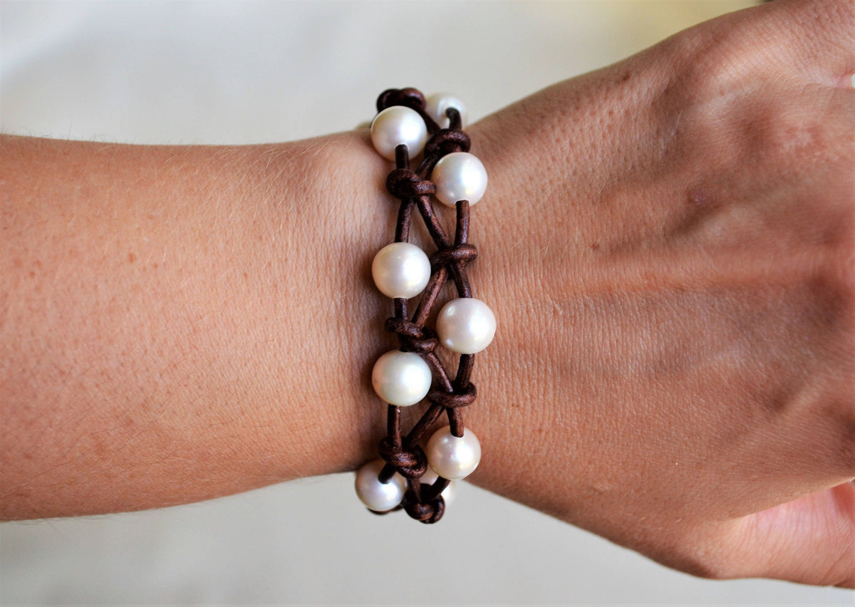Bracelet with white beads and brown braided design on a wrist against a neutral background
