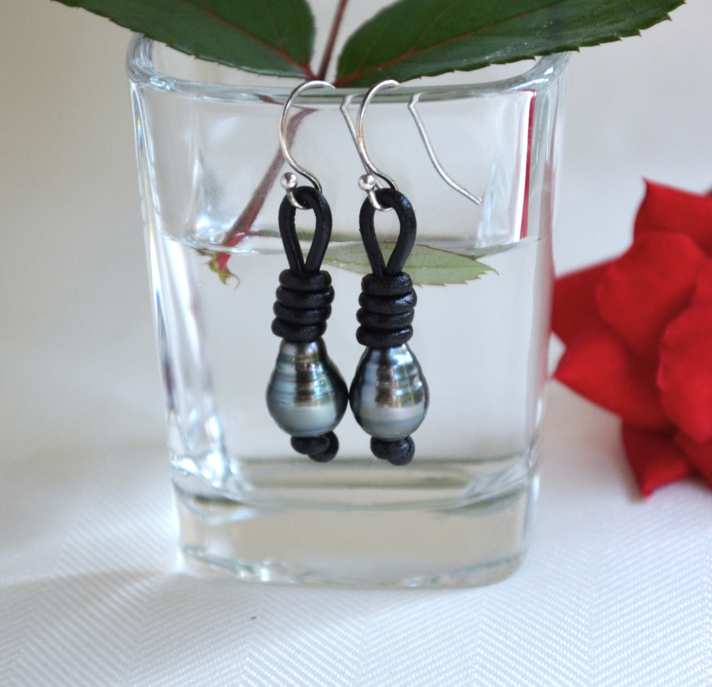 Black Tahitian pearls and sterling silver earrings hanging from a glass vase with a red flower in the background