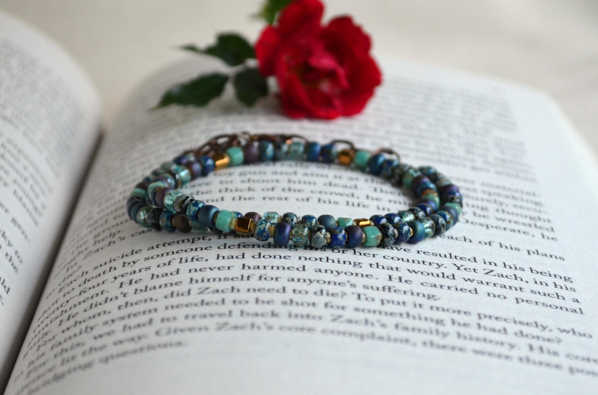 Beaded necklace on an open book with a red rose.