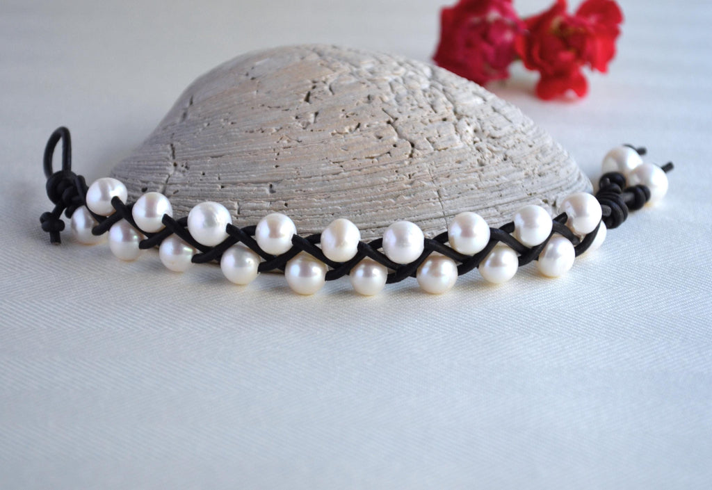 Pearl necklace with black cord on a textured surface with red flowers in the background