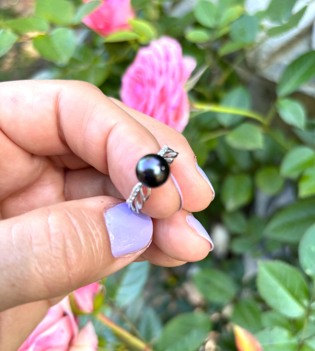 Hand holding a Tahitian Pearl sterling silver ring with green foliage in the background