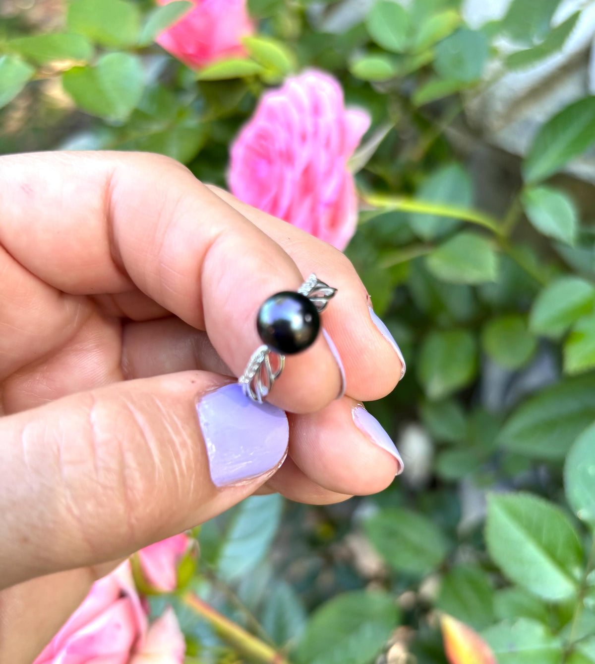 Hand holding a Tahitian Pearl sterling silver ring with green foliage in the background