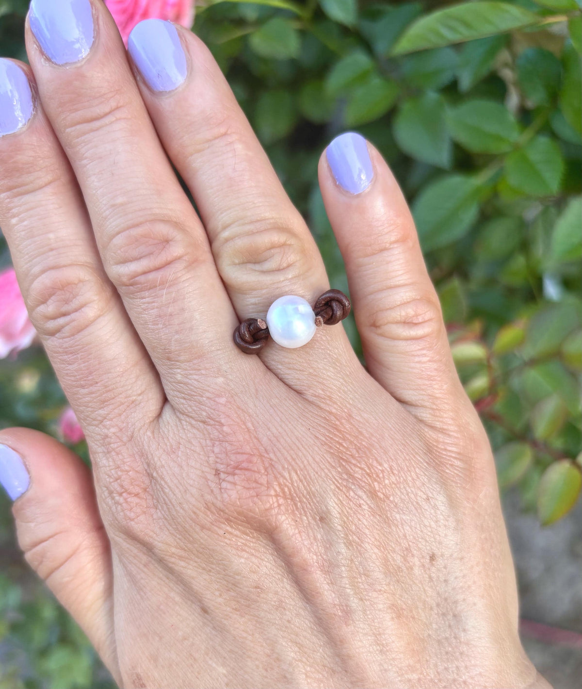 Hand wearing a ring with pearls against a blurred natural background