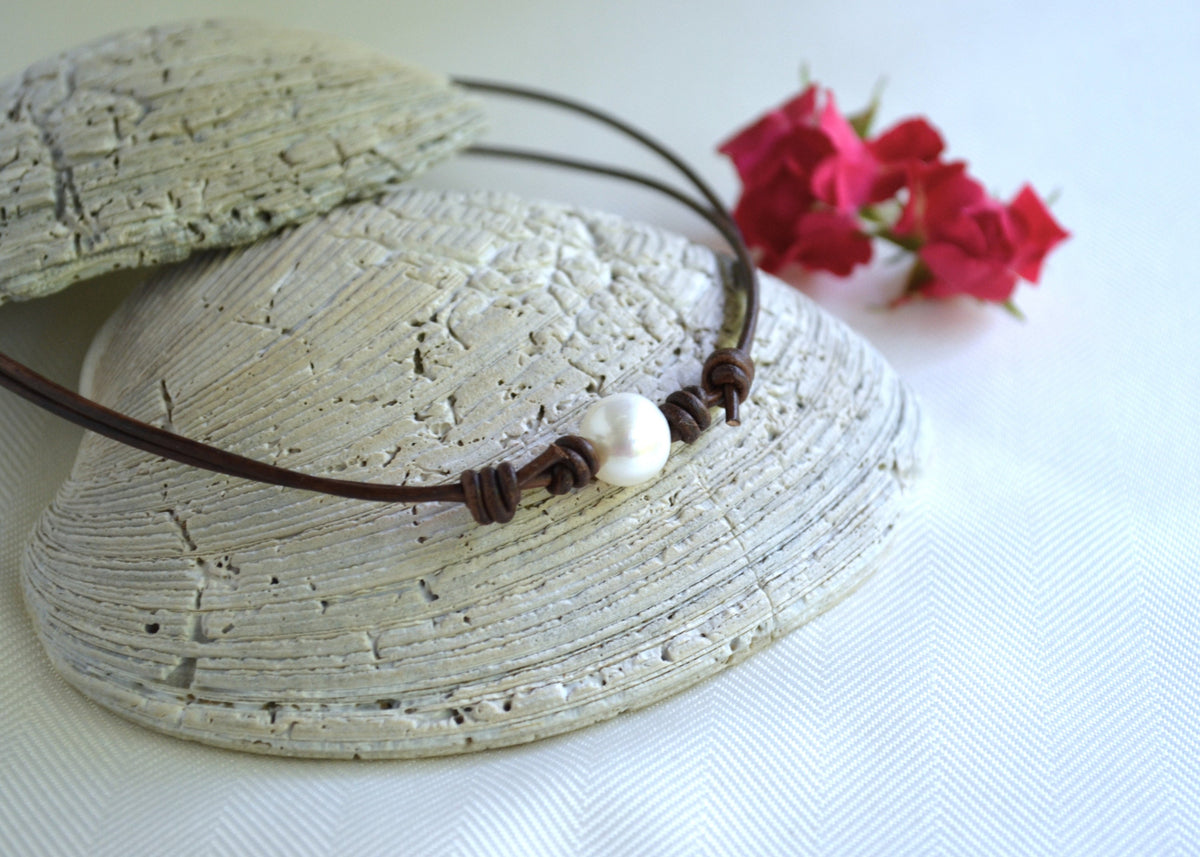 Necklace with a pearl pendant on a textured shell with pink flowers in the background
