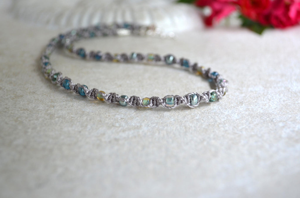 Short necklace with colorful beads on a white surface with flowers in the background