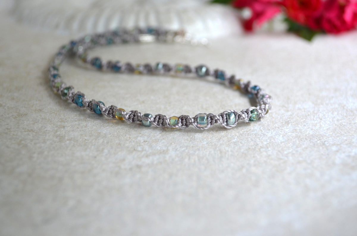 Short necklace with colorful beads on a white surface with flowers in the background