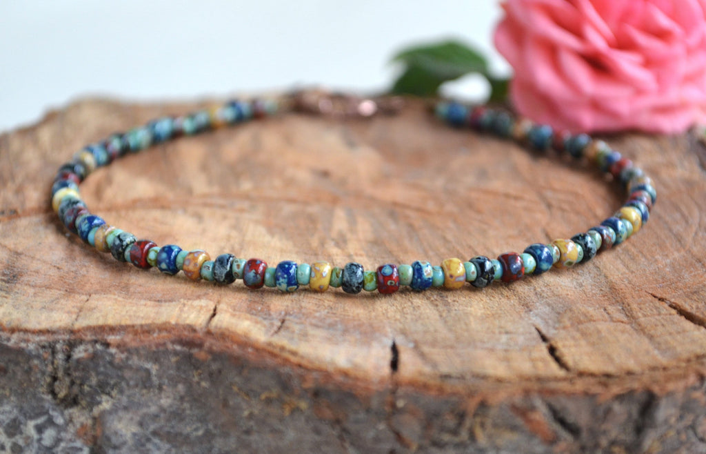 Multicolored beaded anklet on a wooden surface with a pink flower in the background