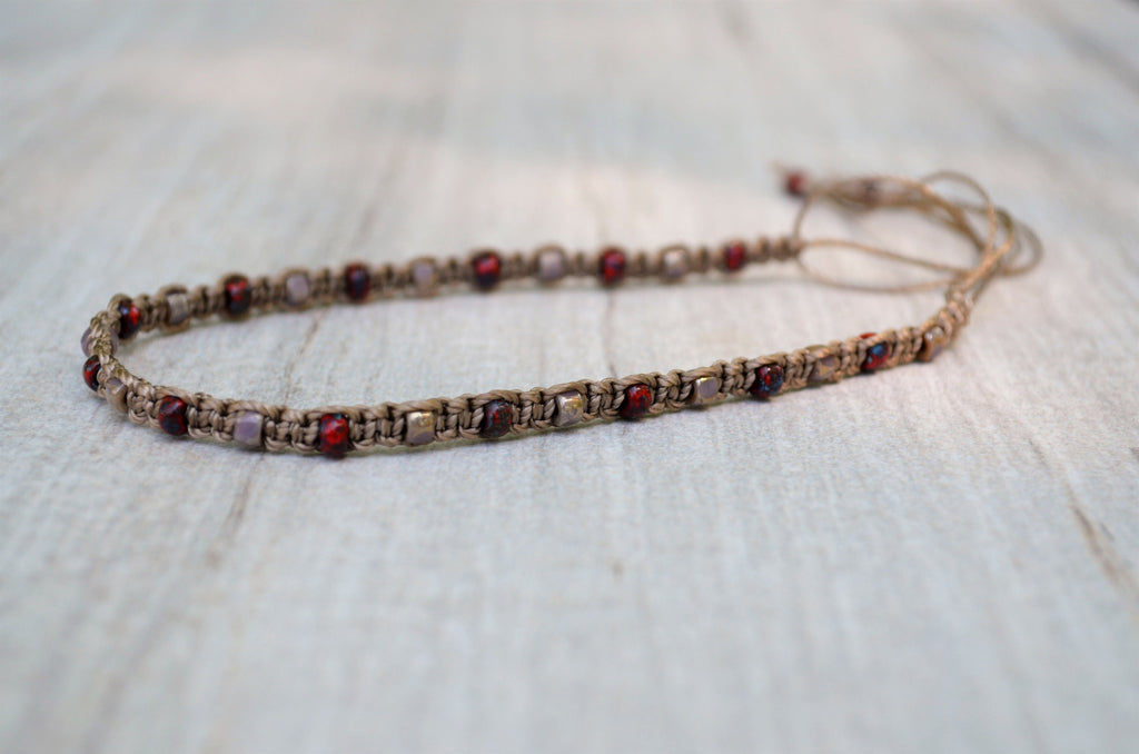 Beaded anklet with red and purple stones on a textured surface