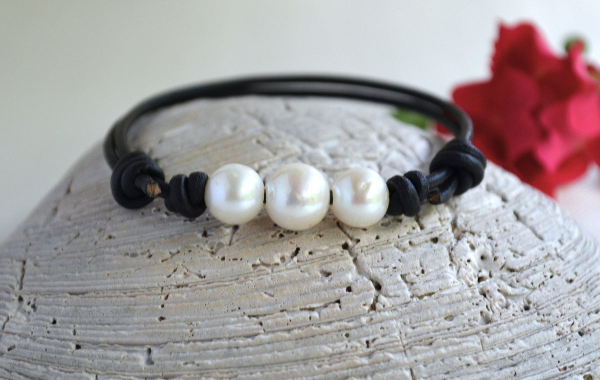 Leather bracelet with white freshwater pearls on a textured surface with a red flower in the background