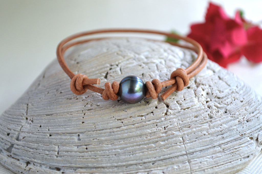 Bracelet with a black pearl on a wooden surface with red flowers in the background