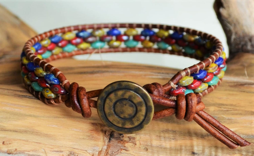 Multicolored beaded bracelet with a brown leather strap and metal button on a wooden surface.