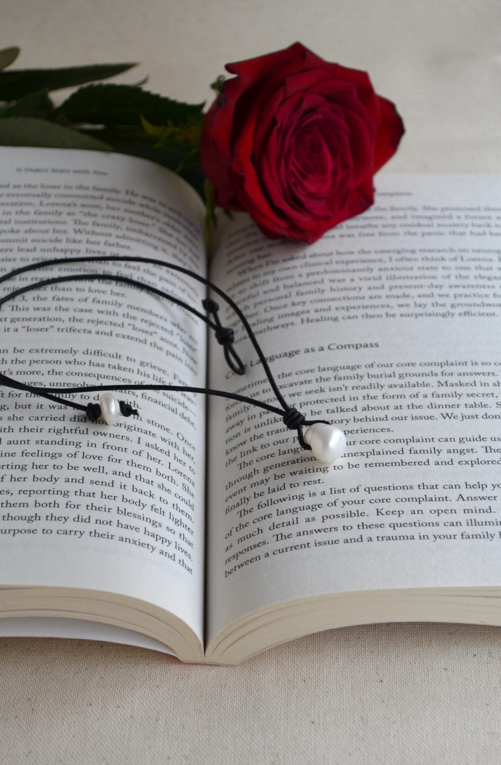 Open book with a red rose on top and a black necklace with white pearls.