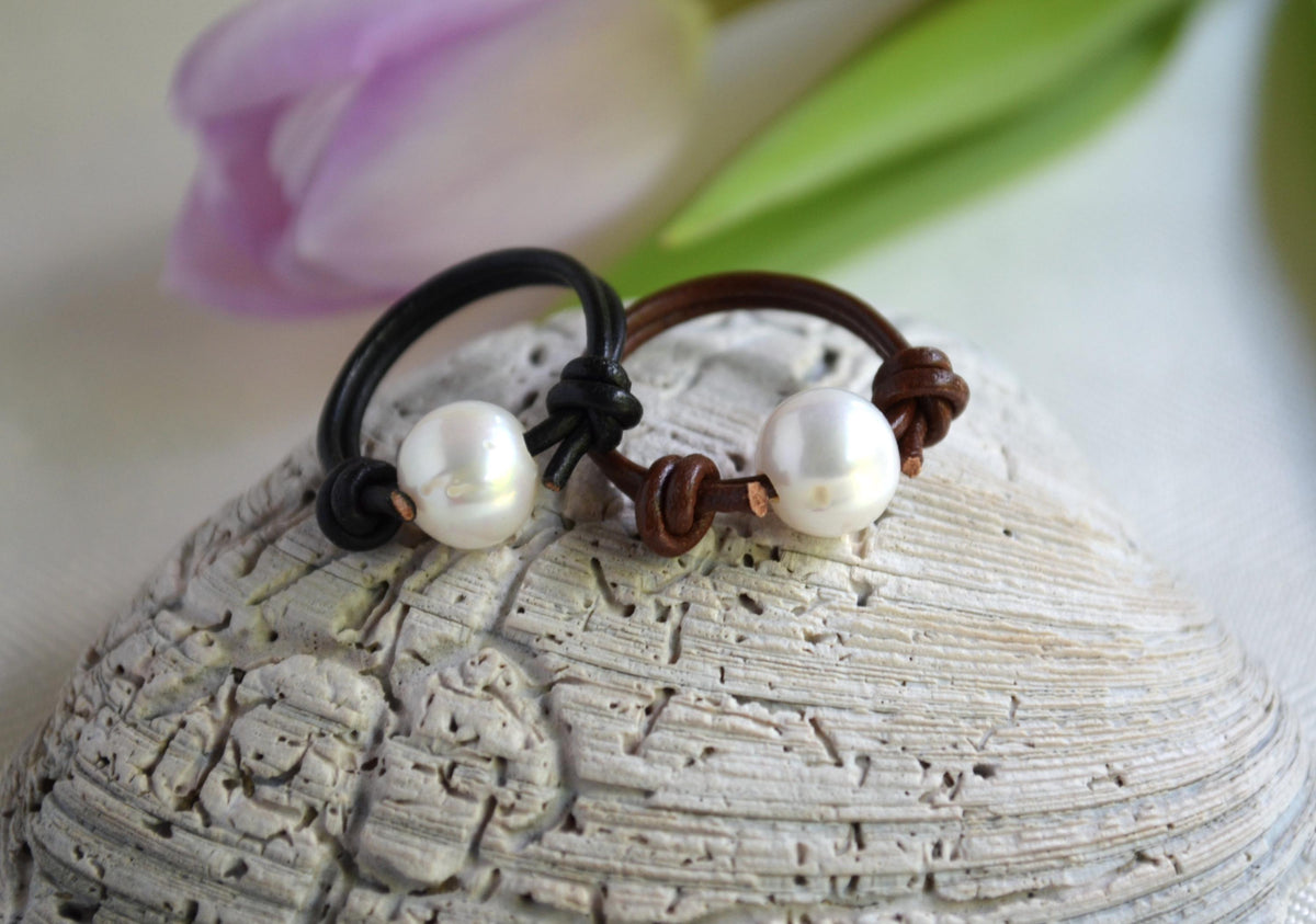 Two pearl rings on a textured stone surface with flowers in the background