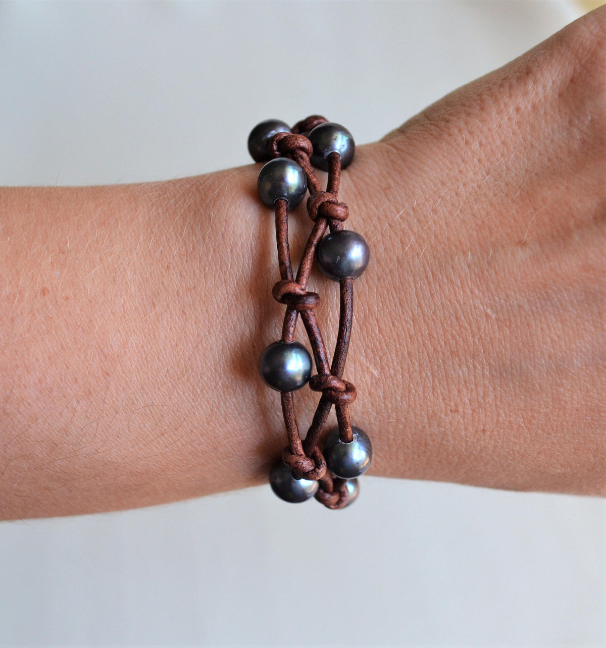 Bracelet with peacock freshwater pearls and brown leather straps on a wrist against a white background