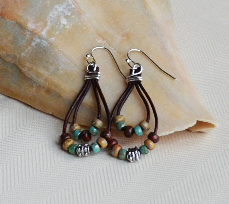 Pair of beaded earrings with brown leather straps on a stone surface