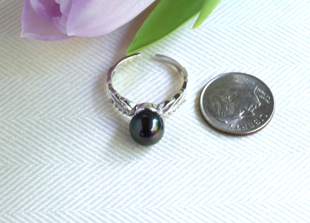 Silver ring with a black Tahitian pearl next to a quarter on a white fabric background