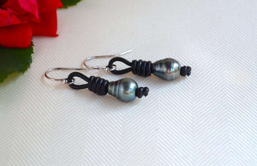 Pair of black Tahitian pearls earrings on a white fabric background with a red flower.