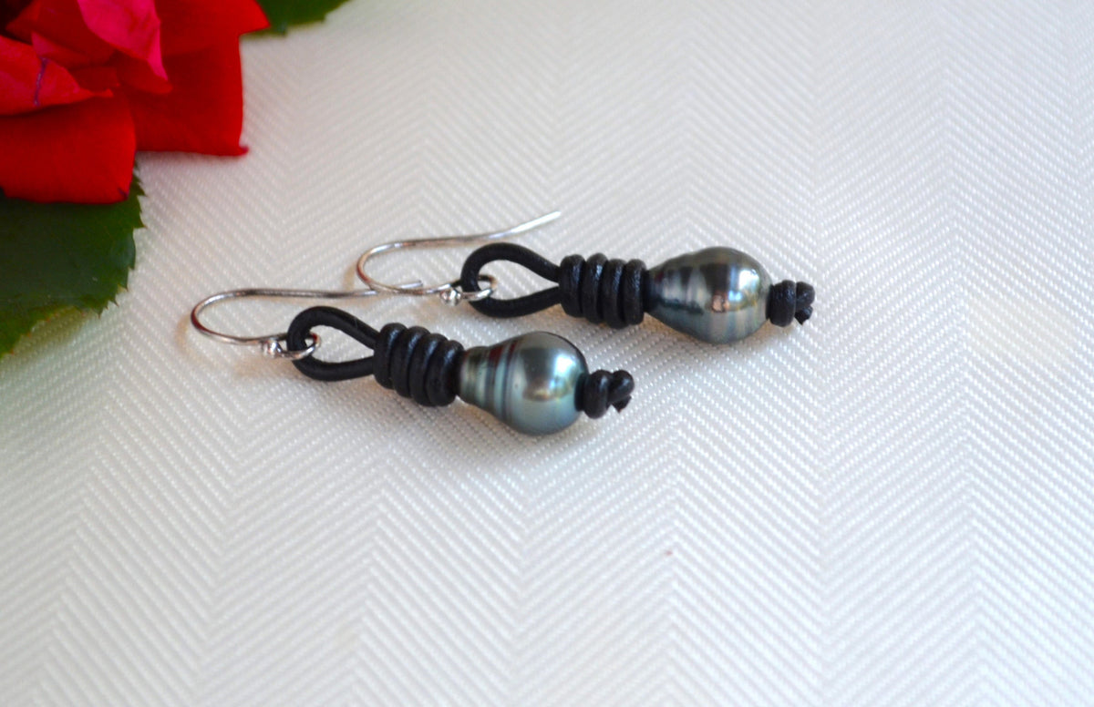 Pair of black Tahitian pearls earrings on a white fabric background with a red flower.