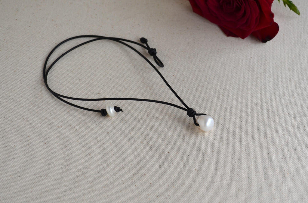 Pearl necklace on a black cord with a red rose in the background on a light gray surface