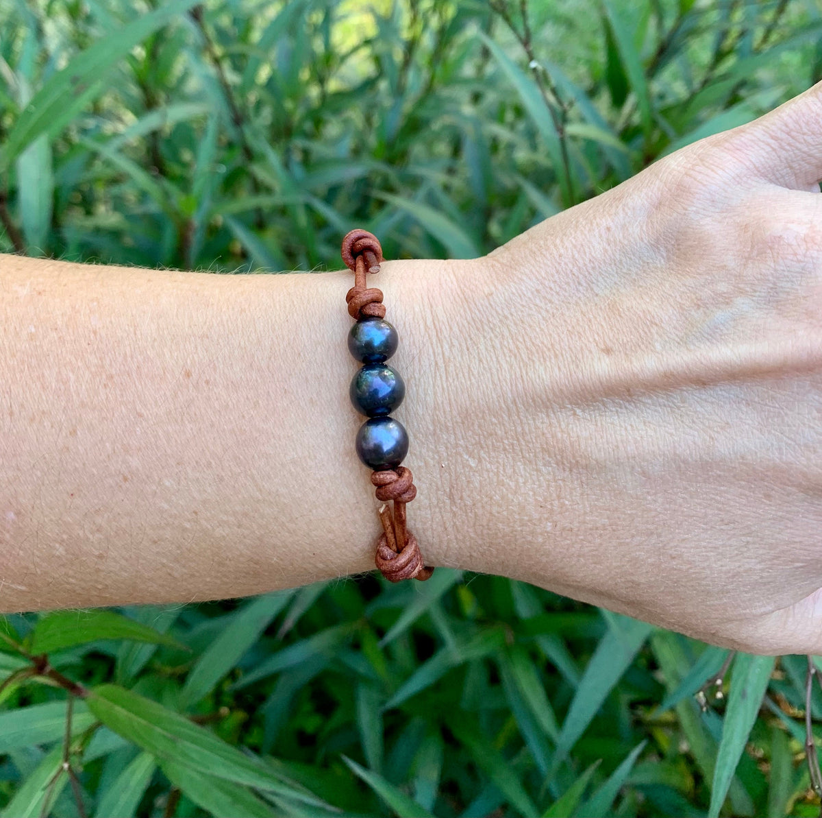 Bracelet with blue pearls beads on a wrist against a green leafy background