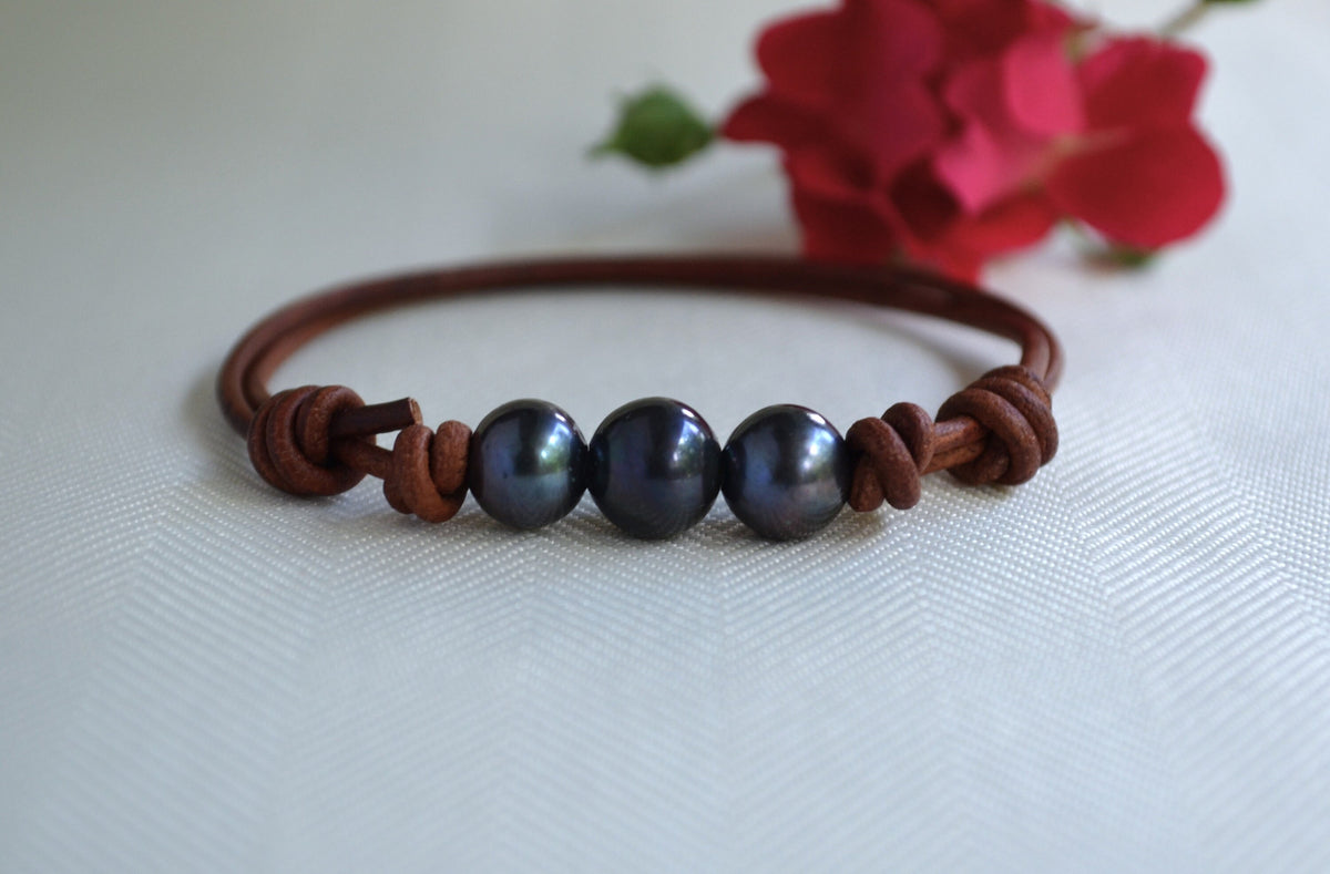 Bracelet with dark pearls and brown leather strap on a light background