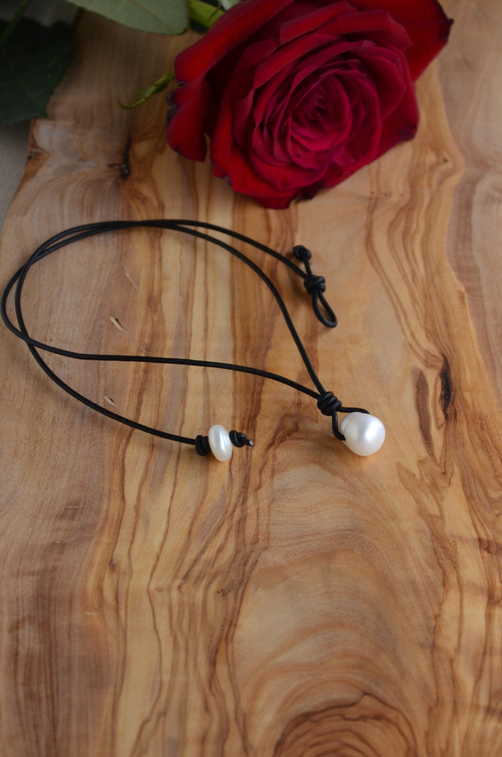Necklace with white pearls on a black cord on a wooden surface with a red rose.