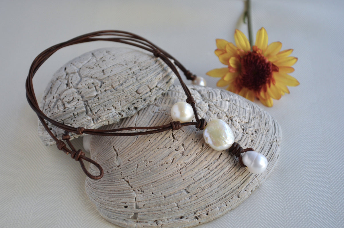 Pearl necklace with brown cord on a textured stone surface with a yellow flower.