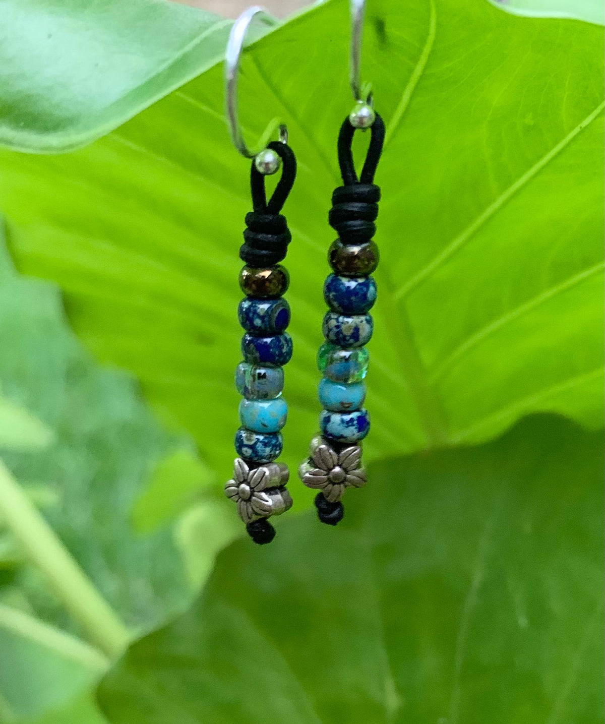 Beaded earrings with floral charms on a green leaf background
