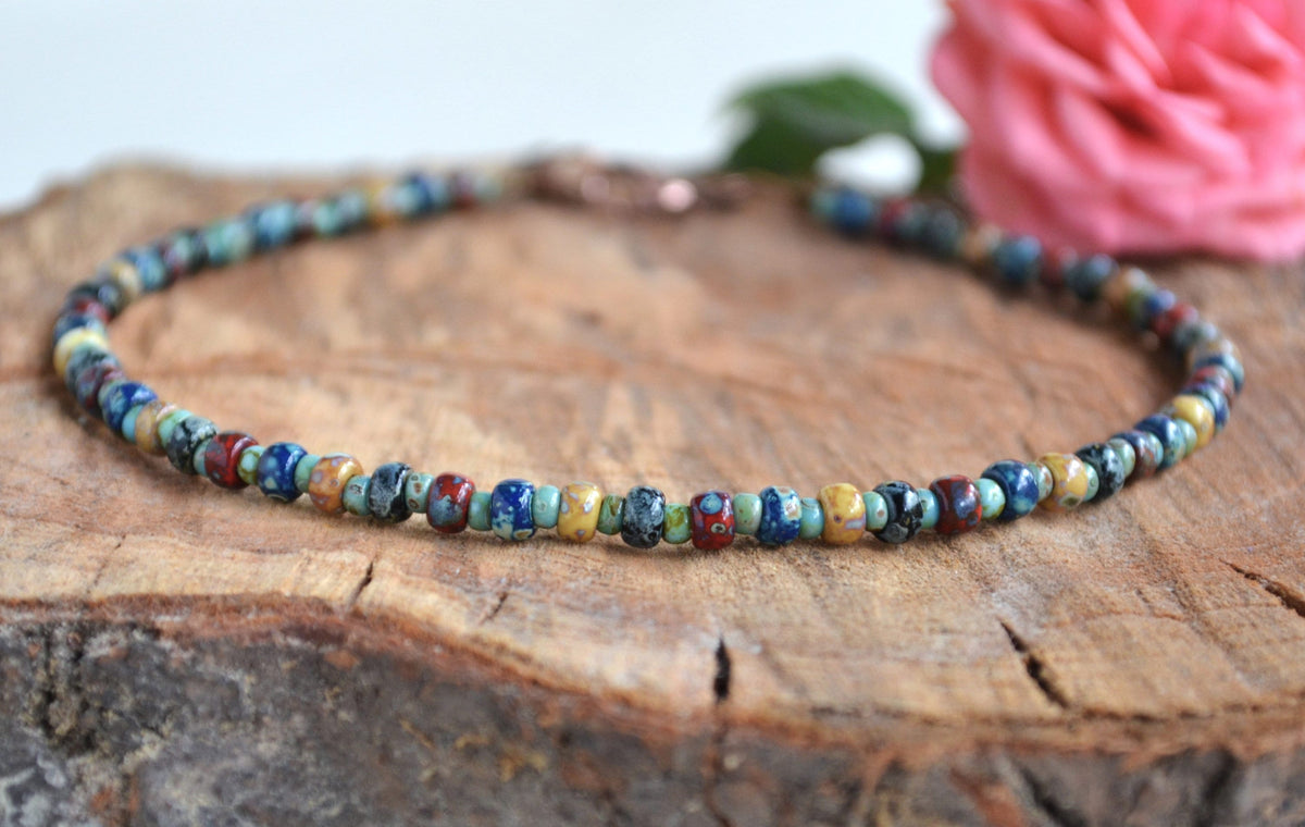 Multicolored beaded anklet on a wooden surface with a blurred pink flower in the background
