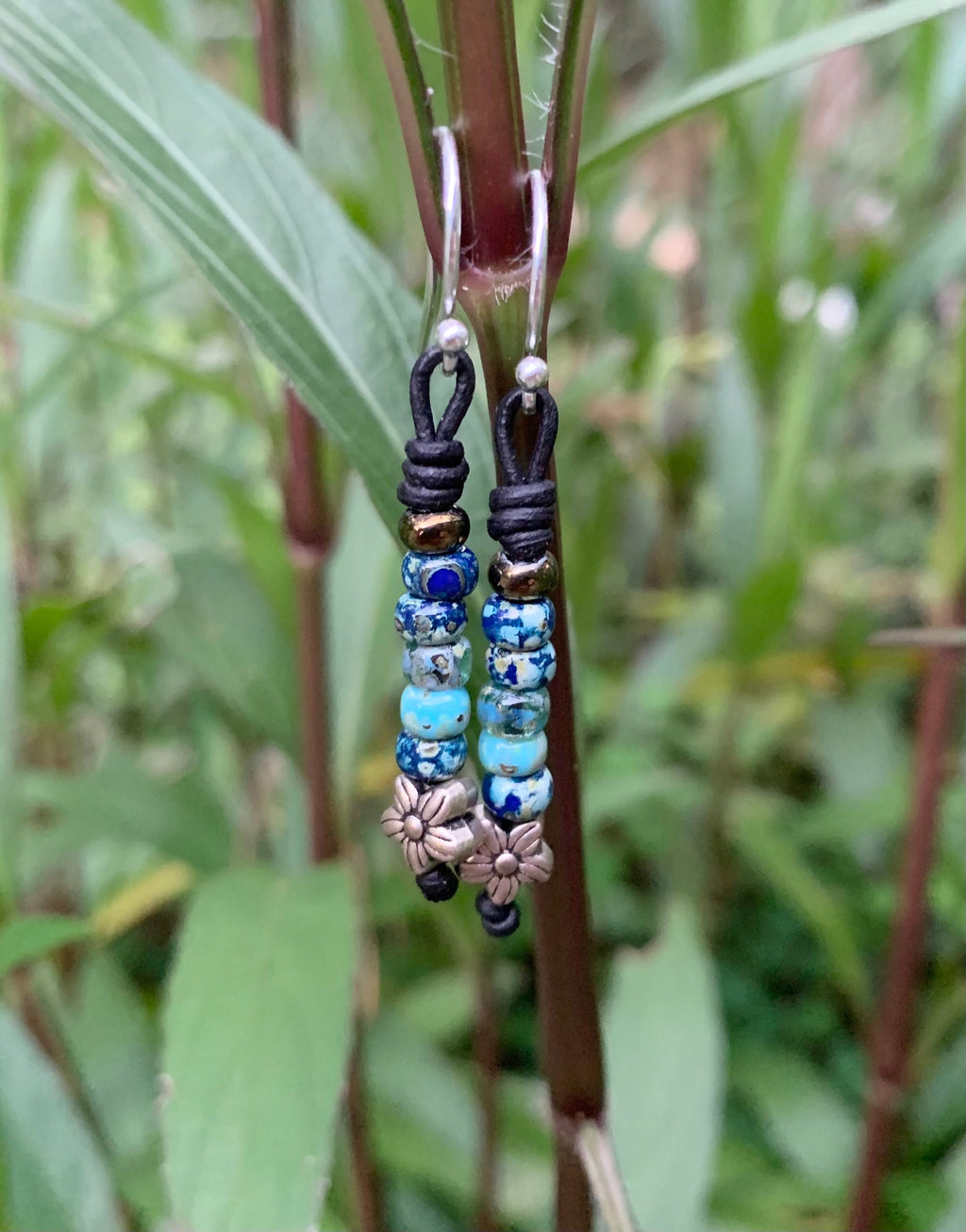 Beaded earrings hanging from a plant with a natural background