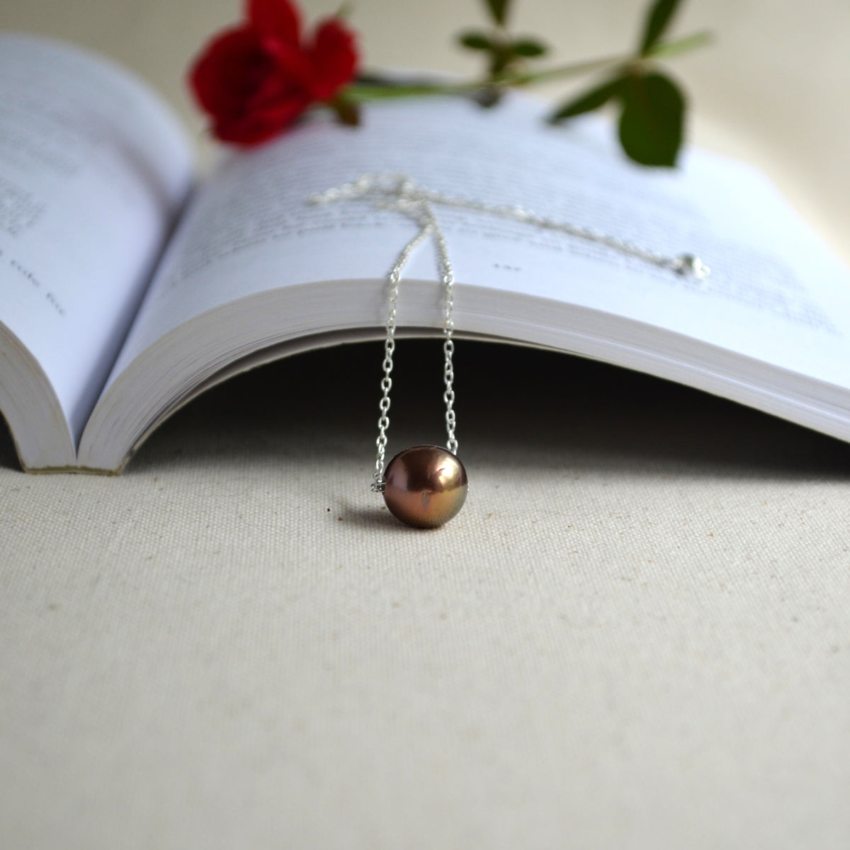 Floating Edison pearl necklace hanging in front of open book, chocolate bronze pearl with warm luster