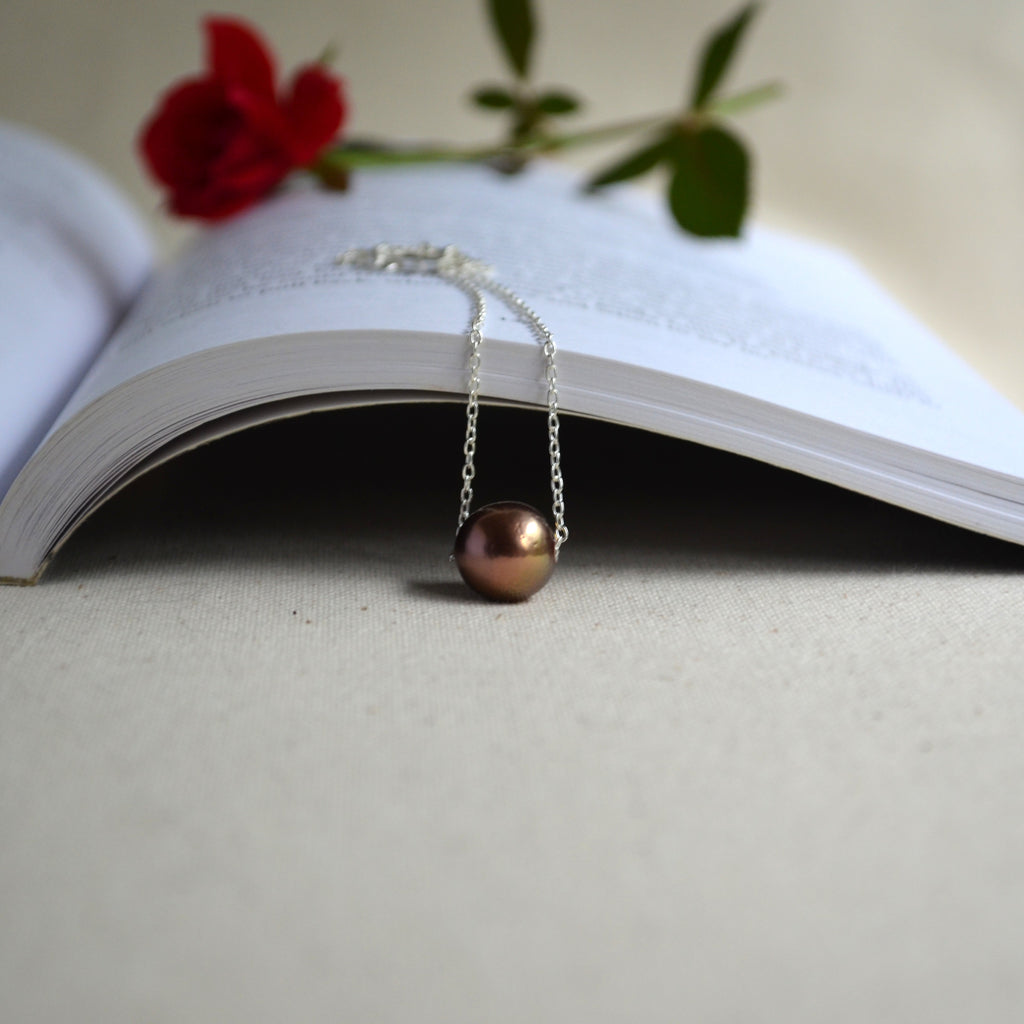 Floating Edison pearl necklace hanging in front of open book, chocolate bronze pearl with warm luster